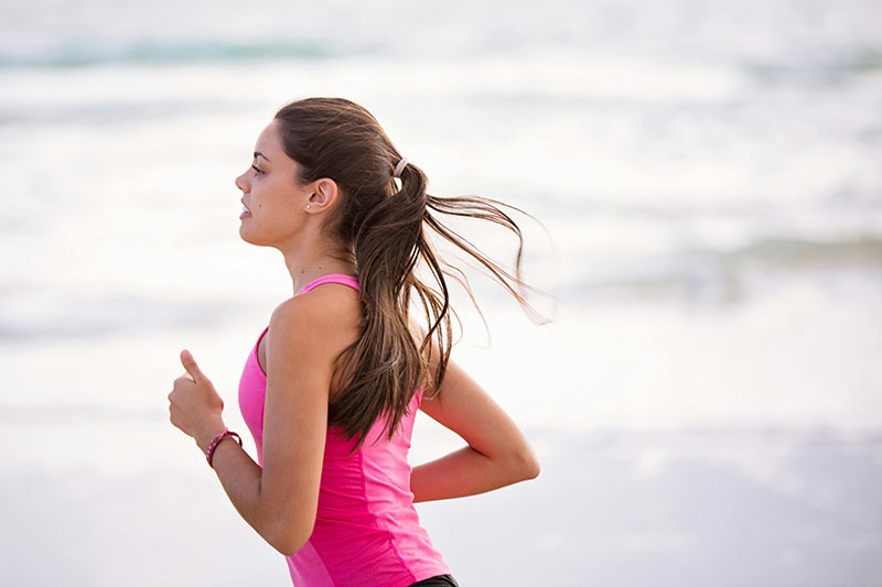 young woman in pink tank running on the beach